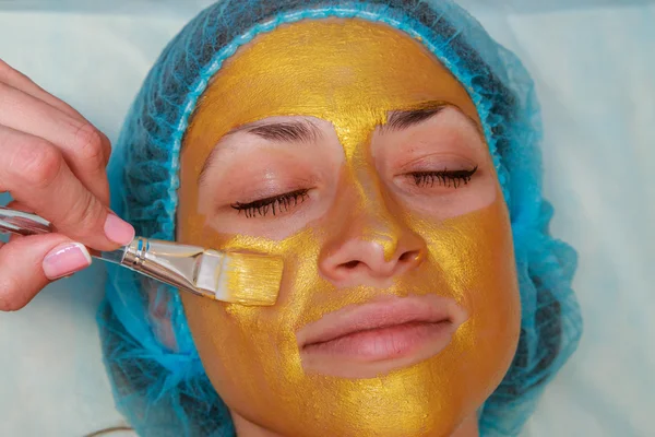 Aplicação de máscaras douradas no rosto do modelo. Procedimentos cosméticos — Fotografia de Stock