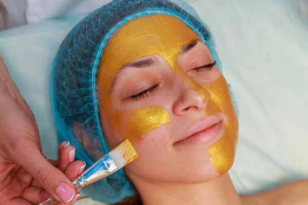 Aplicación de máscaras doradas en la cara del modelo. Procedimientos cosméticos — Foto de Stock