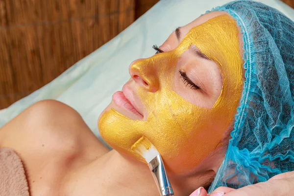 Application of golden masks on the face of the model. Cosmetic procedures — Stock Photo, Image