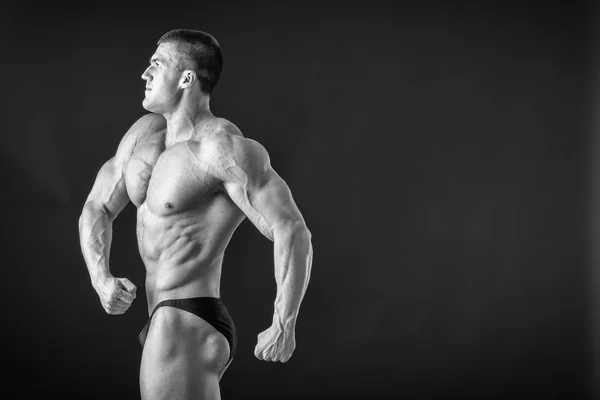 Fisiculturista posando em diferentes poses demonstrando seus músculos. Falha num fundo escuro. Homem mostrando músculos se esforçando. Bonito atleta corpo muscular . — Fotografia de Stock