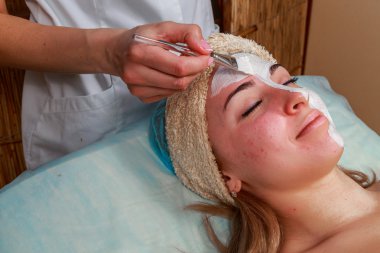 Güzellik salonunda güzellik uzmanı olan bir kız. Güzellik uzmanı kozmetik işlemleri yapıyor. Kozmetik krem uyguluyor. Kozmetoloji, yüz bakımı, güzellik yüz bakımı kavramı. Kozmetoloji hakkında makale.