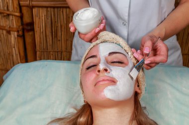 Güzellik salonunda güzellik uzmanı olan bir kız. Güzellik uzmanı kozmetik işlemleri yapıyor. Kozmetik krem uyguluyor. Kozmetoloji, yüz bakımı, güzellik yüz bakımı kavramı. Kozmetoloji hakkında makale.