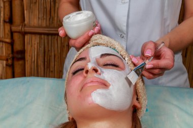 Güzellik salonunda güzellik uzmanı olan bir kız. Güzellik uzmanı kozmetik işlemleri yapıyor. Kozmetik krem uyguluyor. Kozmetoloji, yüz bakımı, güzellik yüz bakımı kavramı. Kozmetoloji hakkında makale.