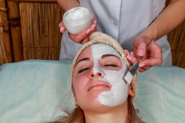 Güzellik salonunda güzellik uzmanı olan bir kız. Güzellik uzmanı kozmetik işlemleri yapıyor. Kozmetik krem uyguluyor. Kozmetoloji, yüz bakımı, güzellik yüz bakımı kavramı. Kozmetoloji hakkında makale.