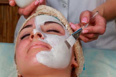 Güzellik salonunda güzellik uzmanı olan bir kız. Güzellik uzmanı kozmetik işlemleri yapıyor. Kozmetik krem uyguluyor. Kozmetoloji, yüz bakımı, güzellik yüz bakımı kavramı. Kozmetoloji hakkında makale.