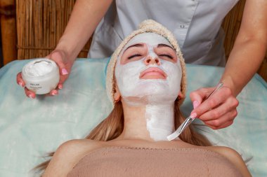 Bir genç kızın yüzüne maske uygulanıyor. Spa salonu yüz cilt