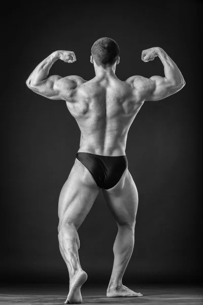 Fisiculturista posando em diferentes poses demonstrando seus músculos. Falha num fundo escuro. Homem mostrando músculos se esforçando. Bonito atleta corpo muscular . — Fotografia de Stock