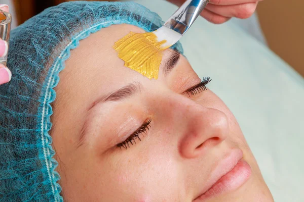 Aplicación de máscaras doradas en la cara del modelo. Procedimientos cosméticos —  Fotos de Stock