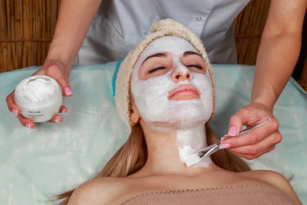 Aplicando la máscara a la cara de una joven. Piel facial en el salón de spa —  Fotos de Stock