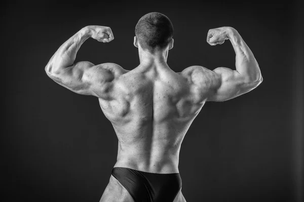 Fisiculturista posando em diferentes poses demonstrando seus músculos. Falha num fundo escuro. Homem mostrando músculos se esforçando. Bonito atleta corpo muscular . — Fotografia de Stock