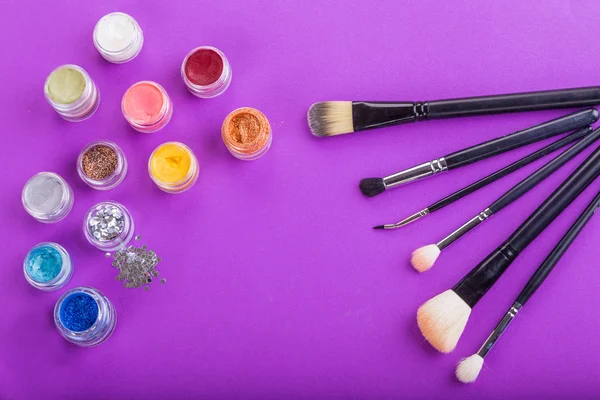 Фарби, пензлі та інші інструменти макіяж на фіолетовому фоні — стокове фото