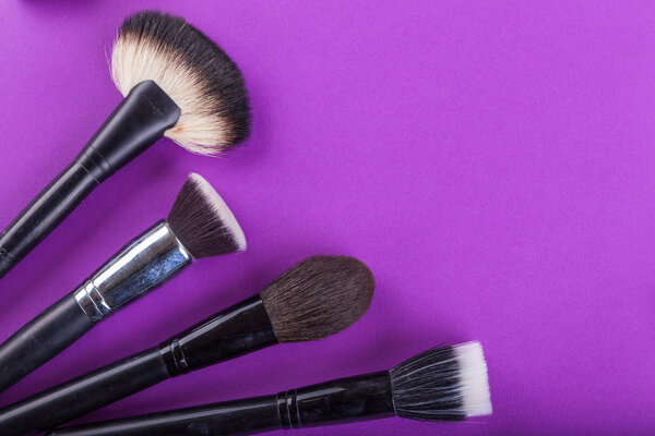 Краски, кисти и другие инструменты макияж на фиолетовом фоне
