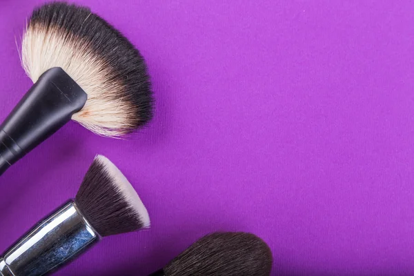 Фарби, пензлі та інші інструменти макіяж на фіолетовому фоні — стокове фото