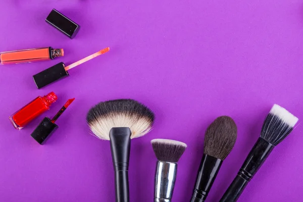 Farby, pędzle i inne narzędzia makijaż na fioletowym tle — Zdjęcie stockowe