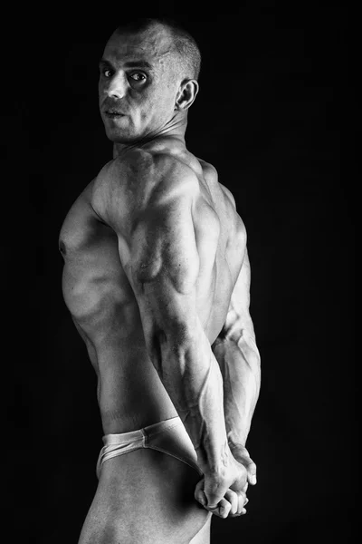 Culturist care prezintă în diferite poziții care demonstrează mușchii lor. Eșecul pe un fundal întunecat. Bărbat care arată tensiunea musculară. Frumos atlet al corpului muscular . — Fotografie, imagine de stoc