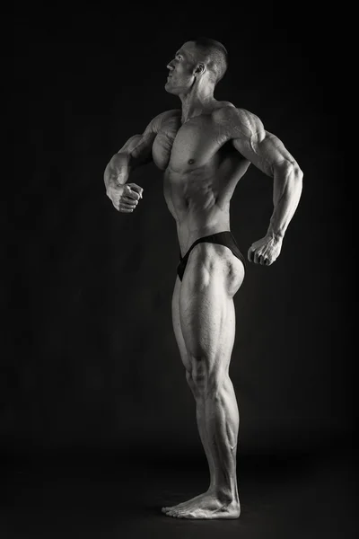 Fisiculturista posando em diferentes poses demonstrando seus músculos. Falha num fundo escuro. Homem mostrando músculos se esforçando. Bonito atleta corpo muscular . — Fotografia de Stock