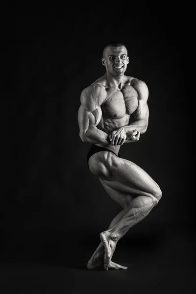 Fisiculturista posando em diferentes poses demonstrando seus músculos. Falha num fundo escuro. Homem mostrando músculos se esforçando. Bonito atleta corpo muscular . — Fotografia de Stock