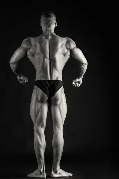 Fisiculturista posando em diferentes poses demonstrando seus músculos. Falha num fundo escuro. Homem mostrando músculos se esforçando. Bonito atleta corpo muscular . — Fotografia de Stock