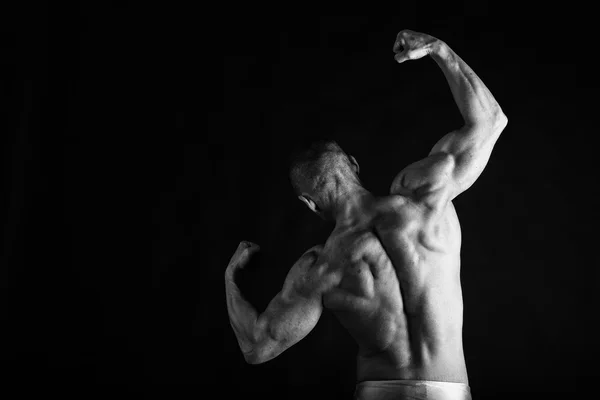 Kulturista pózuje v různých pózách, prokazující jejich svaly. Neúspěch na tmavém pozadí. Mužské zobrazeno svaly napínat. Krásné svalnaté tělo sportovce. — Stock fotografie
