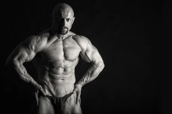 Fisiculturista posando em diferentes poses demonstrando seus músculos. Falha num fundo escuro. Homem mostrando músculos se esforçando. Bonito atleta corpo muscular . — Fotografia de Stock