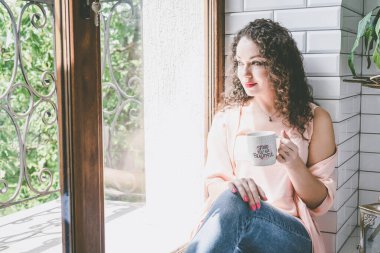 Pencerenin yanında kupası olan güzel bir kız.