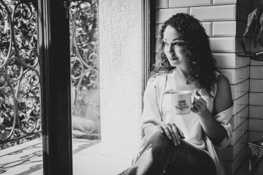 Pencerenin yanında kupası olan güzel bir kız.