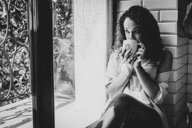 Pencerenin yanında kupası olan güzel bir kız.