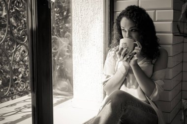 Pencerenin yanında kupası olan güzel bir kız.