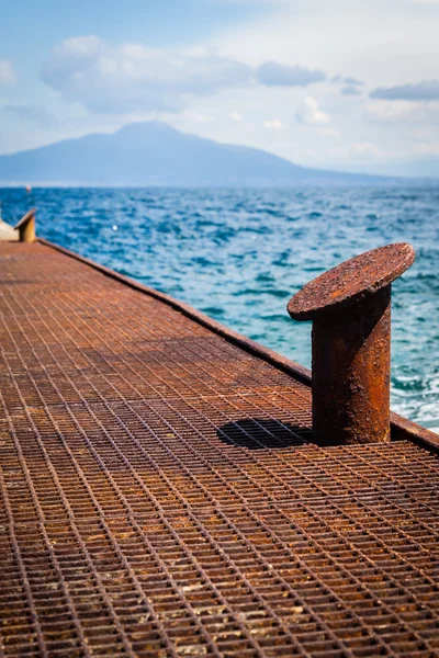 Old rusty bollard on pier with water — Stock Photo, Image