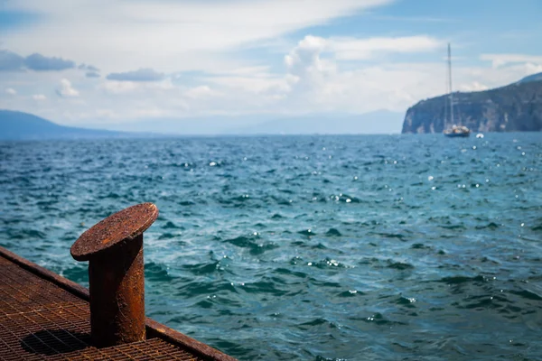 Old rusty bollard on pier with water — Stock Photo, Image