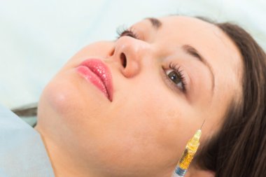 Güzellik uzmanı hastanın yüz içine enjeksiyon yapar