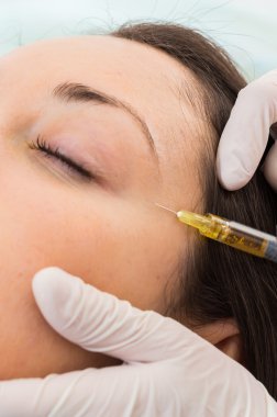 Güzellik uzmanı hastanın yüz içine enjeksiyon yapar