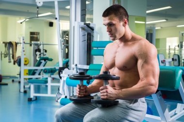 Adam spor salonunda dambıllarla egzersiz yapıyor.