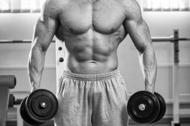 Adam spor salonunda dambıllarla egzersiz yapıyor.