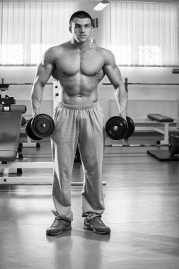 Adam spor salonunda dambıllarla egzersiz yapıyor.