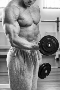 Adam spor salonunda dambıllarla egzersiz yapıyor.