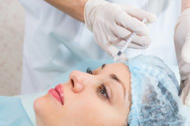 Güzellik uzmanı hastanın yüz içine enjeksiyon yapar