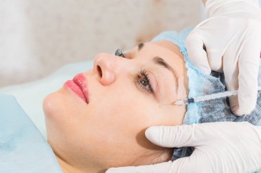 Güzellik uzmanı hastanın yüz içine enjeksiyon yapar