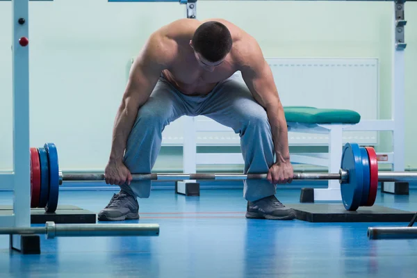 Hombre haciendo ejercicios con una barra en el gimnasio — Foto de Stock