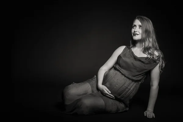 En gravid kvinna på en mörk bakgrund — Stockfoto