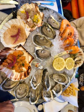 Seafood platter with oysters, scallops, shrimp and tartare served on ice with lemon slices.