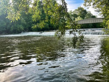 Açık mavi göl, görünür su altı kayaları ve parlak bir gökyüzünün altında sakin bir yüzey..