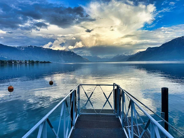 Sakin bir dağ gölünde, durgun sularda çarpıcı bulutlar ve yansımalarla manzaralı bir iskele..