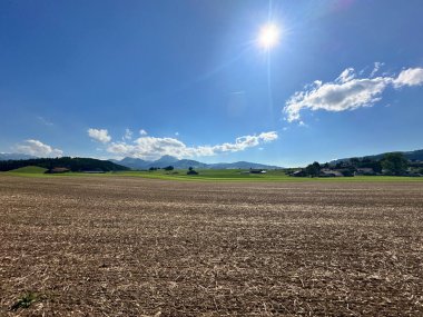 Parlak mavi gökyüzünün altında yeşil tarlalar ve dağlar.