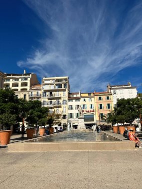 Mavi gökyüzünün altında heykeli, çeşmesi ve geleneksel binaları olan renkli Avrupa meydanı.