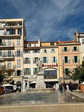 Mavi gökyüzünün altında heykeli, çeşmesi ve geleneksel binaları olan renkli Avrupa meydanı.