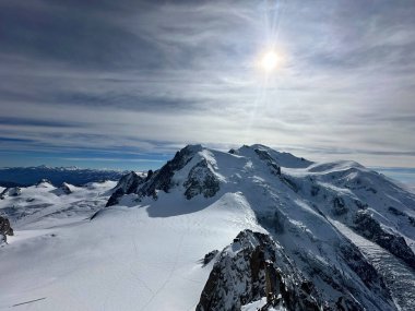 Karlı Mont Blanc yığını, dramatik buzullar ve yumuşak bulutlu gökyüzünün altında engebeli tepeler..