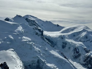 Karlı Mont Blanc yığını, dramatik buzullar ve yumuşak bulutlu gökyüzünün altında engebeli tepeler..