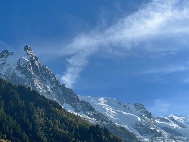 Fransa 'nın Chamonix kentindeki açık mavi gökyüzünün altında Aiguille du Midi' nin karla kaplı zirvesi alp ormanlarının üzerinde yükseliyor..