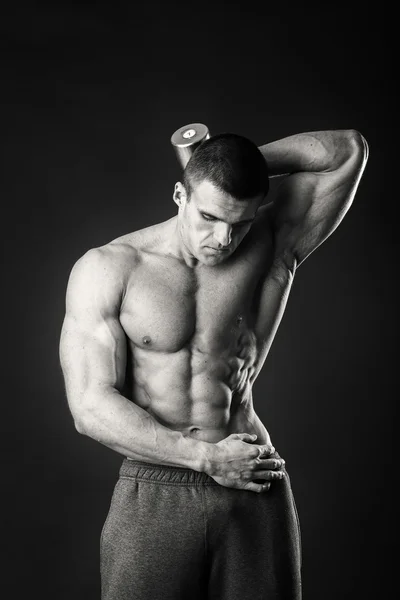 Muscular hombre toma ejercicios con mancuernas sobre un fondo oscuro —  Fotos de Stock